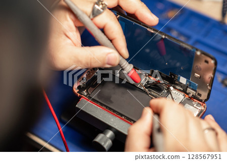 Expert performs smartphone battery repair with precision tools at a tech workshop 128567951