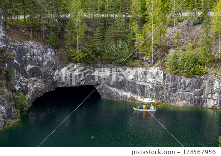 A small boat floats on the tranquil waters of Marble Canyon while surrounded by towering cliffs and lush greenery in Karelia 128567956