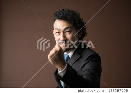 A motivated and energetic middle-aged businessman in a suit posing with a fist in the air against a brown background A fighting businessman 128567996