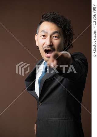 A motivated and energetic middle-aged businessman wearing a suit on a brown background, aiming to be No. 1 and pointing his finger. A fighting businessman 128567997