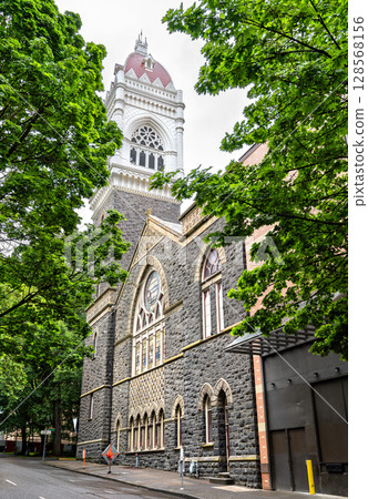 Gothic Revival First Congregational Church in downtown Portland, Oregon, showcasing its striking bell tower and intricate stone facade framed by leafy green trees 128568156