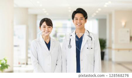 Smiling Asian doctor standing in hospital lobby Smiling Asian doctor standing in hospital lobby 128568276