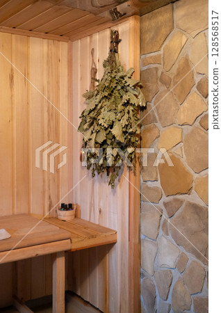 Cozy wooden sauna interior with birch leaves and stone wall Cozy wooden sauna interior with birch leaves and stone wall 128568517