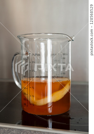 Glass measuring cup with tea and lemon slice on induction stove 128568529