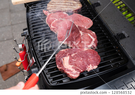 Grilling juicy steaks on outdoor barbecue grill with smoke rising in backyard 128568532