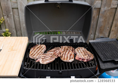 Grilled ribeye steaks on backyard barbecue grill with wooden cutting board 128568533
