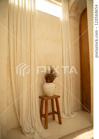 Soft curtains frame a simple vase with dried flowers on a stool Soft curtains frame a simple vase with dried flowers on a stool 128568654