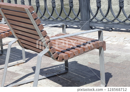 A row of chairs with wooden seats covered with snow near a metal fence on the canal embankment. 128568712
