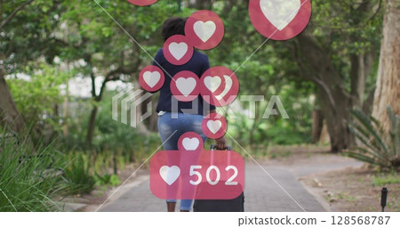 Image of social media heart icons over african american woman riding bicycle in park Image of social media heart icons over african american woman riding bicycle in park 128568787