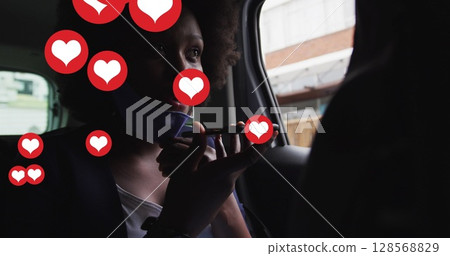 Image of social media heart icons over african american woman with face mask using phone in car 128568829