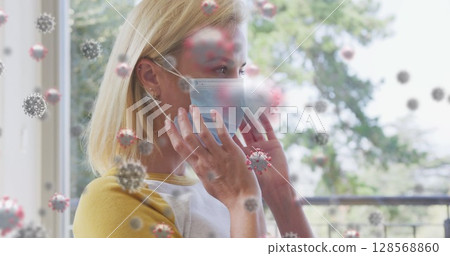 Image of covid 19 cells over caucasian blonde woman putting face mask on 128568860