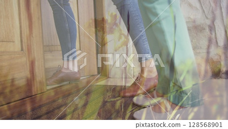 Image of grass moving over midsection of caucasian woman and her daughter opening door 128568901