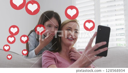 Image of heart icons over caucasian blonde mother and daughter talking on smartphone at home Image of heart icons over caucasian blonde mother and daughter talking on smartphone at home 128568934