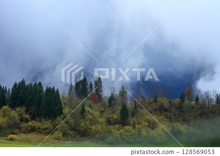 Spooky autumn landscape with foggy mountains at sunset Spooky autumn landscape with foggy mountains at sunset 128569053
