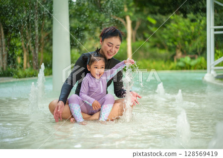 happy mother with toddler girl playing water splashing in swimming pool 128569419