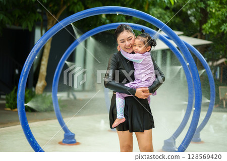 happy mother with toddler girl playing water tunnel splashing in swimming pool 128569420