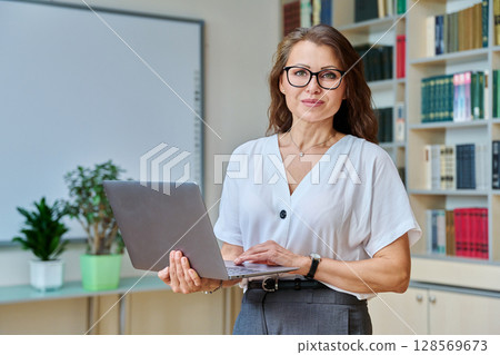 Portrait mature woman teacher, educational behavioral specialist with laptop in classroom Portrait mature woman teacher, educational behavioral specialist with laptop in classroom 128569673