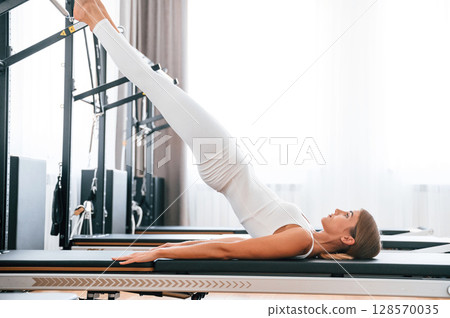 Lying down and stretching legs. Young woman in fitness center is doing exercises Lying down and stretching legs. Young woman in fitness center is doing exercises 128570035