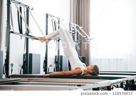 Lying down and stretching legs. Young woman in fitness center is doing exercises Lying down and stretching legs. Young woman in fitness center is doing exercises 128570037