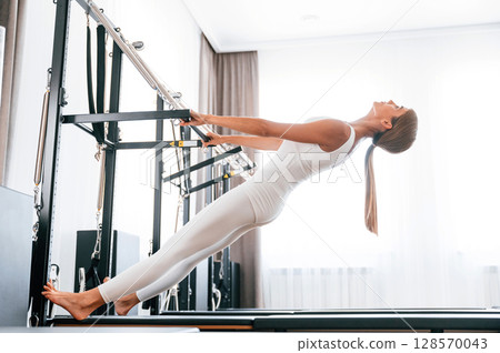 In white sportive clothes. Young woman in fitness center is doing exercises 128570043