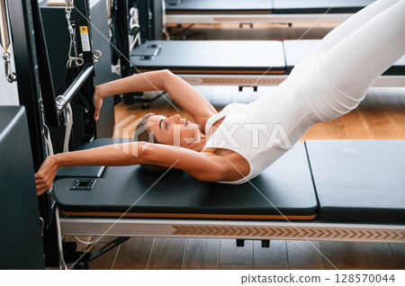 In white sportive clothes. Young woman in fitness center is doing exercises 128570044