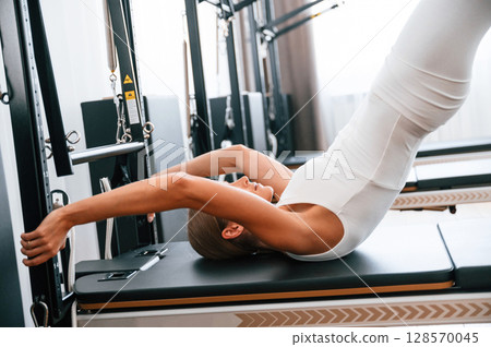 In white sportive clothes. Young woman in fitness center is doing exercises In white sportive clothes. Young woman in fitness center is doing exercises 128570045