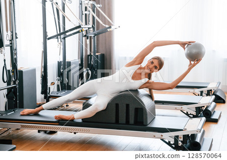 Holding ball in hands. Young woman in fitness center is doing exercises Holding ball in hands. Young woman in fitness center is doing exercises 128570064