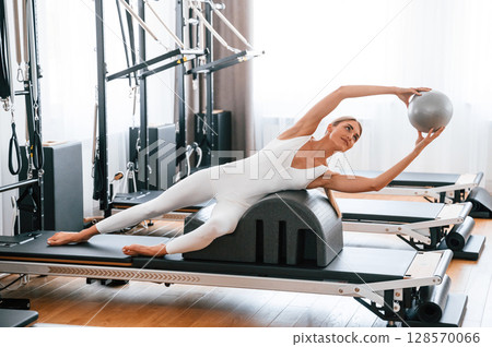 Holding ball in hands. Young woman in fitness center is doing exercises 128570066