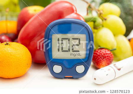 Asian hand holding digital glucose monitor measure with vegetable and fruit healthy food. 128570123