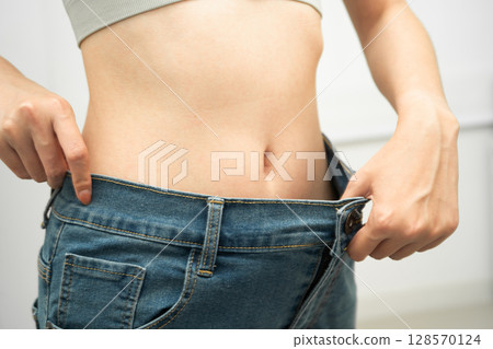Young Asian woman losing weight wearing loose pants in oversize jeans. 128570124