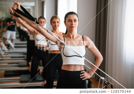 Three women in fitness center are doing exercises Three women in fitness center are doing exercises 128570144