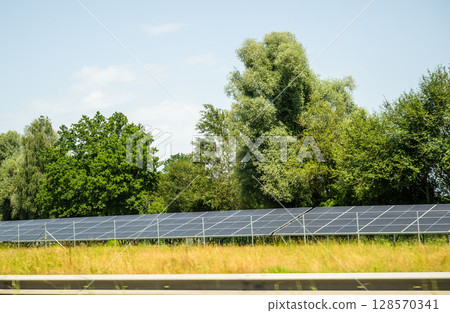 Solar panels in green field near forest on a sunny summer day Solar panels in green field near forest on a sunny summer day 128570341