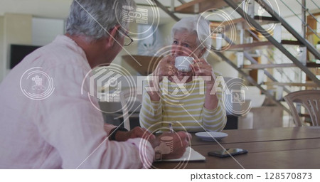 Image of network of connections with icons over senior caucasian couple at home Image of network of connections with icons over senior caucasian couple at home 128570873