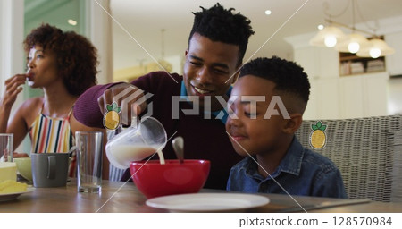 Image of pineapples over happy african american parents and son having breakfast at home Image of pineapples over happy african american parents and son having breakfast at home 128570984