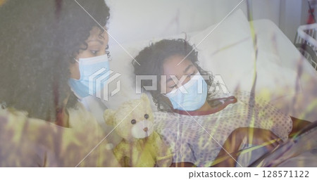 Image of grass over biracial mother with face masks and her daughter lying in hospital Image of grass over biracial mother with face masks and her daughter lying in hospital 128571122