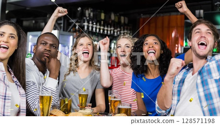 Image of gold confetti falling over happy diverse group of friends drinking in bar 128571198