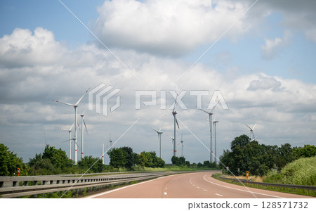 Wind turbines along highway under cloudy sky on summer day, renewable energy landscape Wind turbines along highway under cloudy sky on summer day, renewable energy landscape 128571732