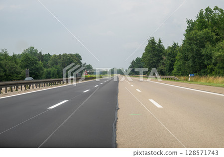 Part of highway newly paved, other part still old surface, partially resurfaced asphalt road 128571743