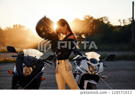 Wearing the protective helmet. Woman is with motorcycle outdoors 128571813