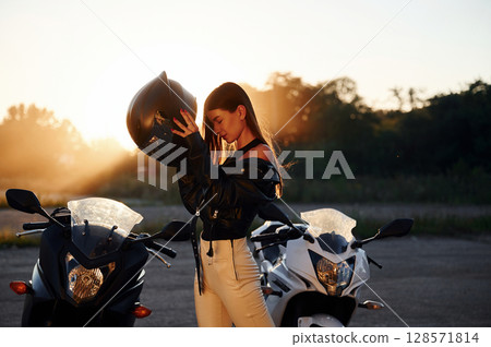 Against beautiful sunlight. Woman is with motorcycle outdoors Against beautiful sunlight. Woman is with motorcycle outdoors 128571814
