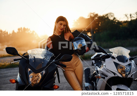 Against beautiful sunlight. Woman is with motorcycle outdoors Against beautiful sunlight. Woman is with motorcycle outdoors 128571815