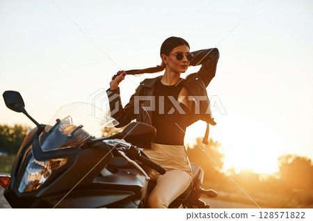 In sunglasses. Woman is with motorcycle outdoors 128571822