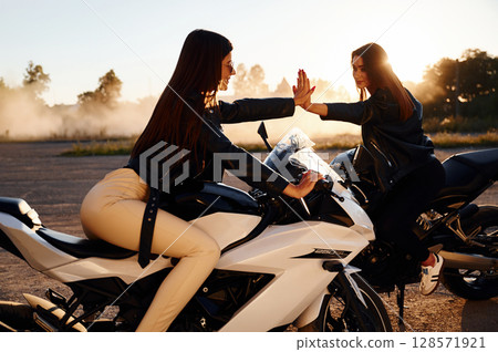 Two women on motorcycles are together outdoors Two women on motorcycles are together outdoors 128571921
