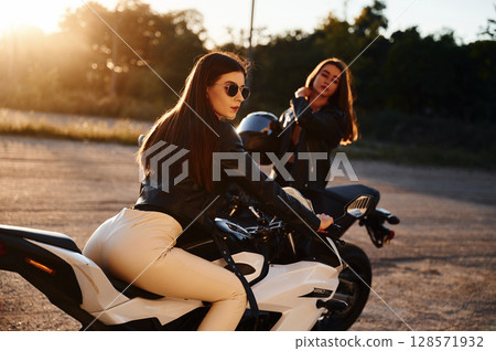 Two women on motorcycles are together outdoors Two women on motorcycles are together outdoors 128571932