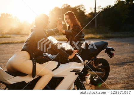 High five gesture. Two women on motorcycles are together outdoors High five gesture. Two women on motorcycles are together outdoors 128571937