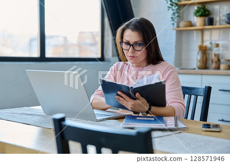 Middle-aged serious woman working at computer laptop in home office 128571946