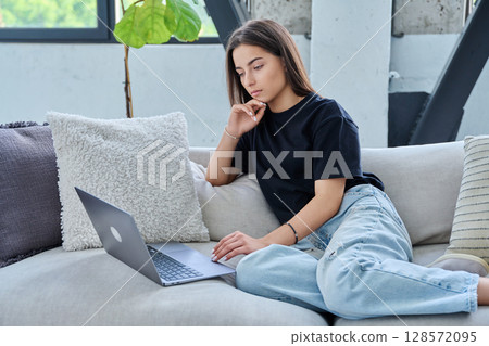 Serious teenage girl looking at laptop, sitting on sofa at home 128572095