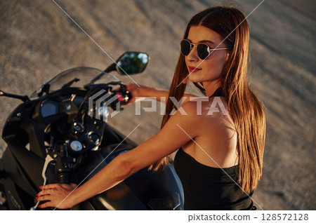 In sunglasses. Woman is with motorcycle outdoors 128572128