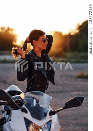 Standing and posing. Woman is with motorcycle outdoors 128572129