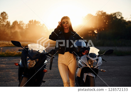 Holding protective helmet in hand. Woman is with motorcycle outdoors Holding protective helmet in hand. Woman is with motorcycle outdoors 128572133